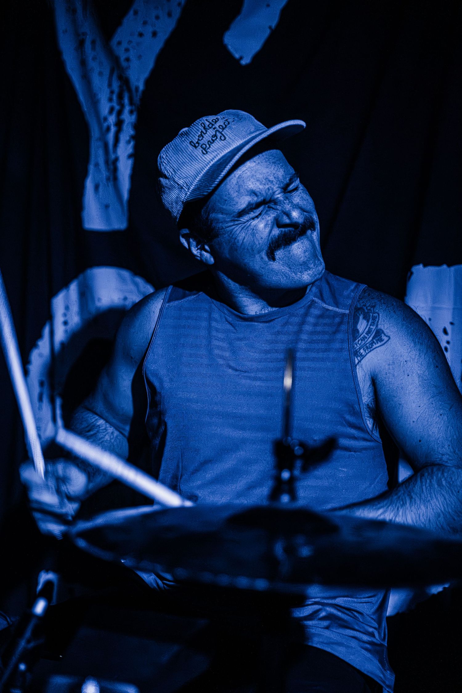 A drummer performs passionately under dramatic blue stage lighting.