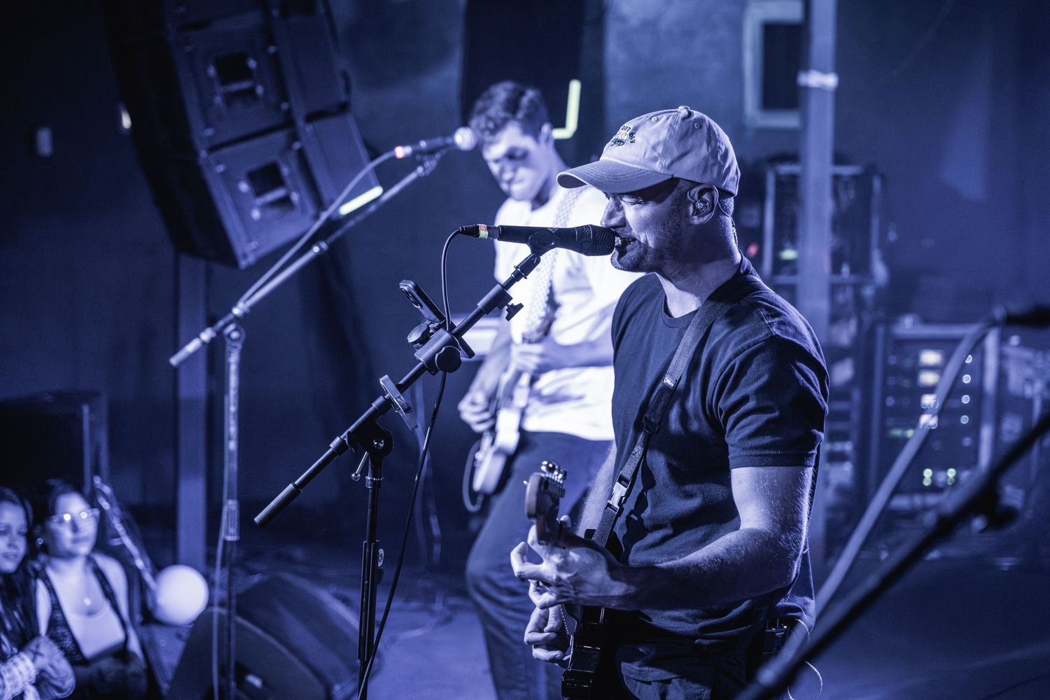 Musicians performing live on stage with dramatic blue lighting and microphone setup.