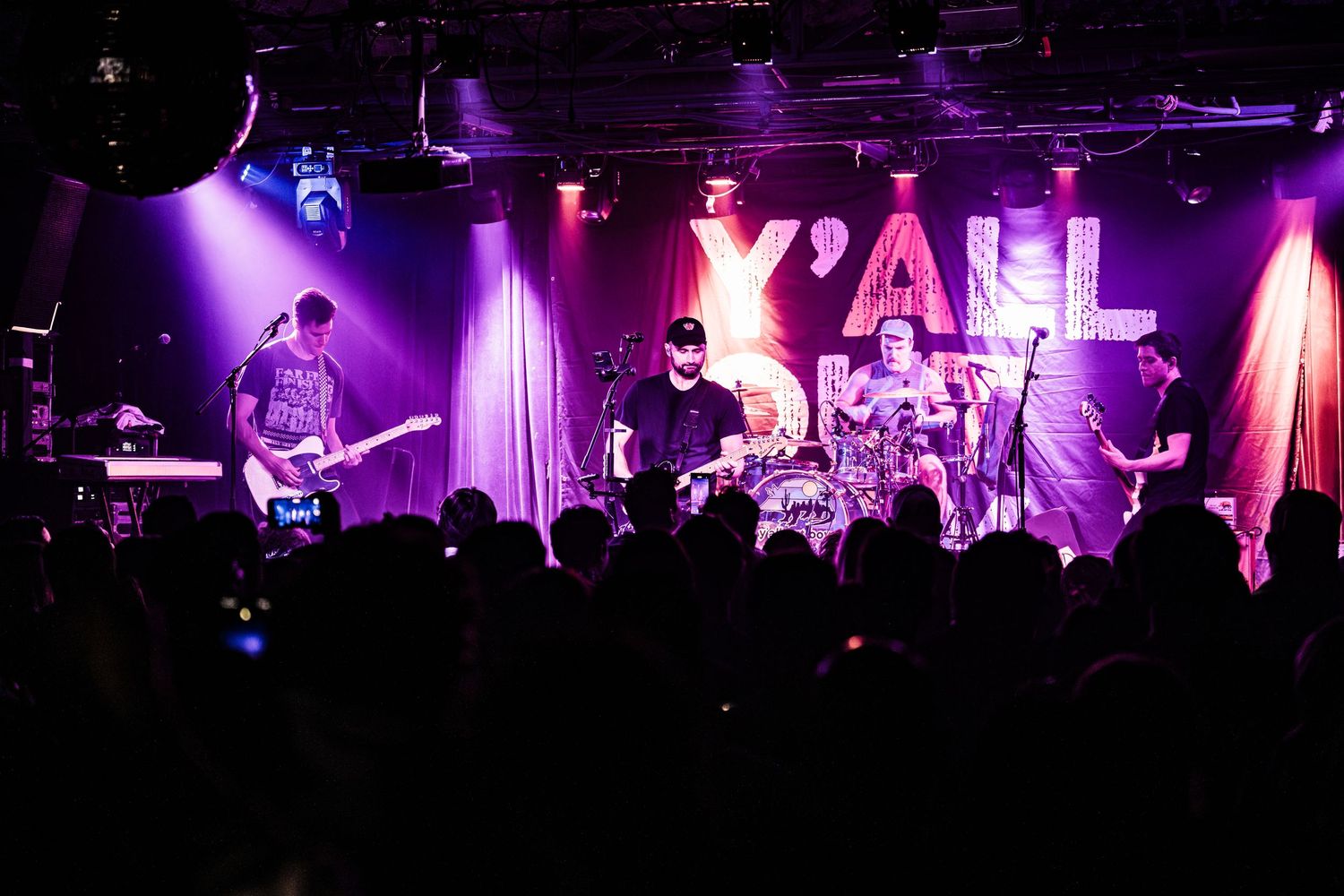 Rock band performing live with purple stage lighting and 'Y'ALL' text display.
