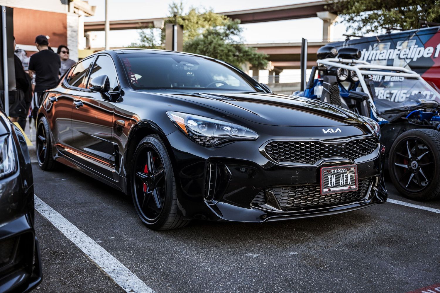 Black Kia Stinger GT with custom wheels parked at an automotive event.