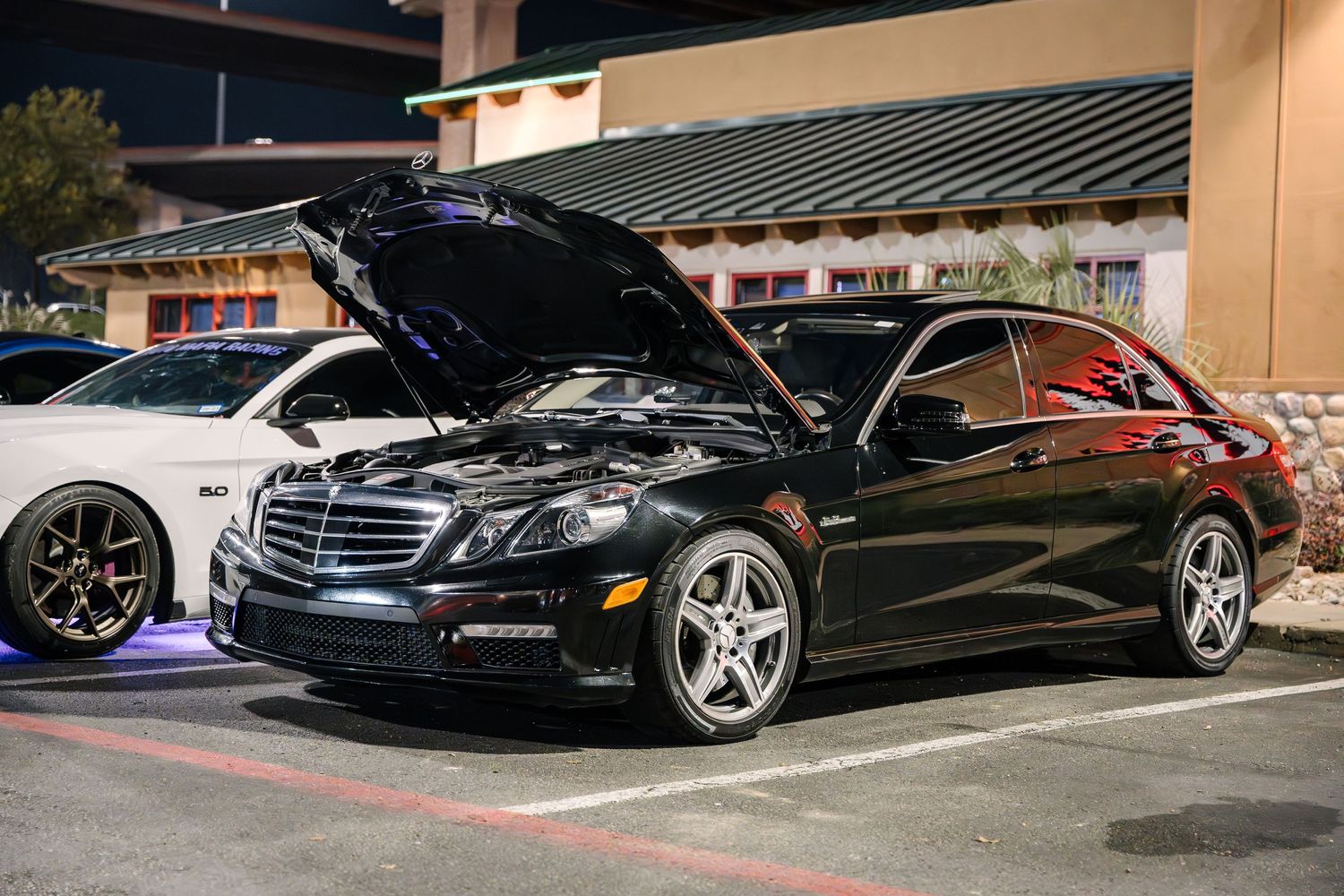 Black Mercedes-Benz E-Class with open hood displayed at a car show.
