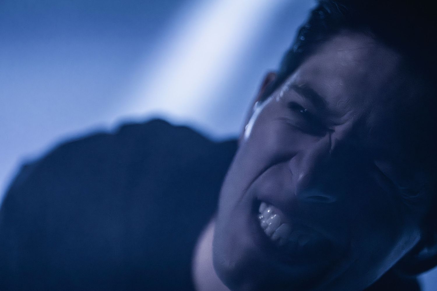 Close-up shot of performer singing passionately under dramatic blue spotlight.