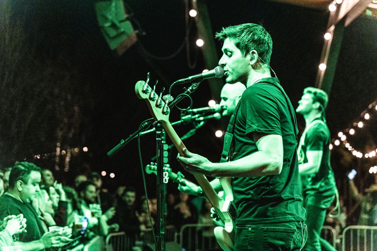 Band performs energetically on stage with dramatic green lighting and crowd in foreground.