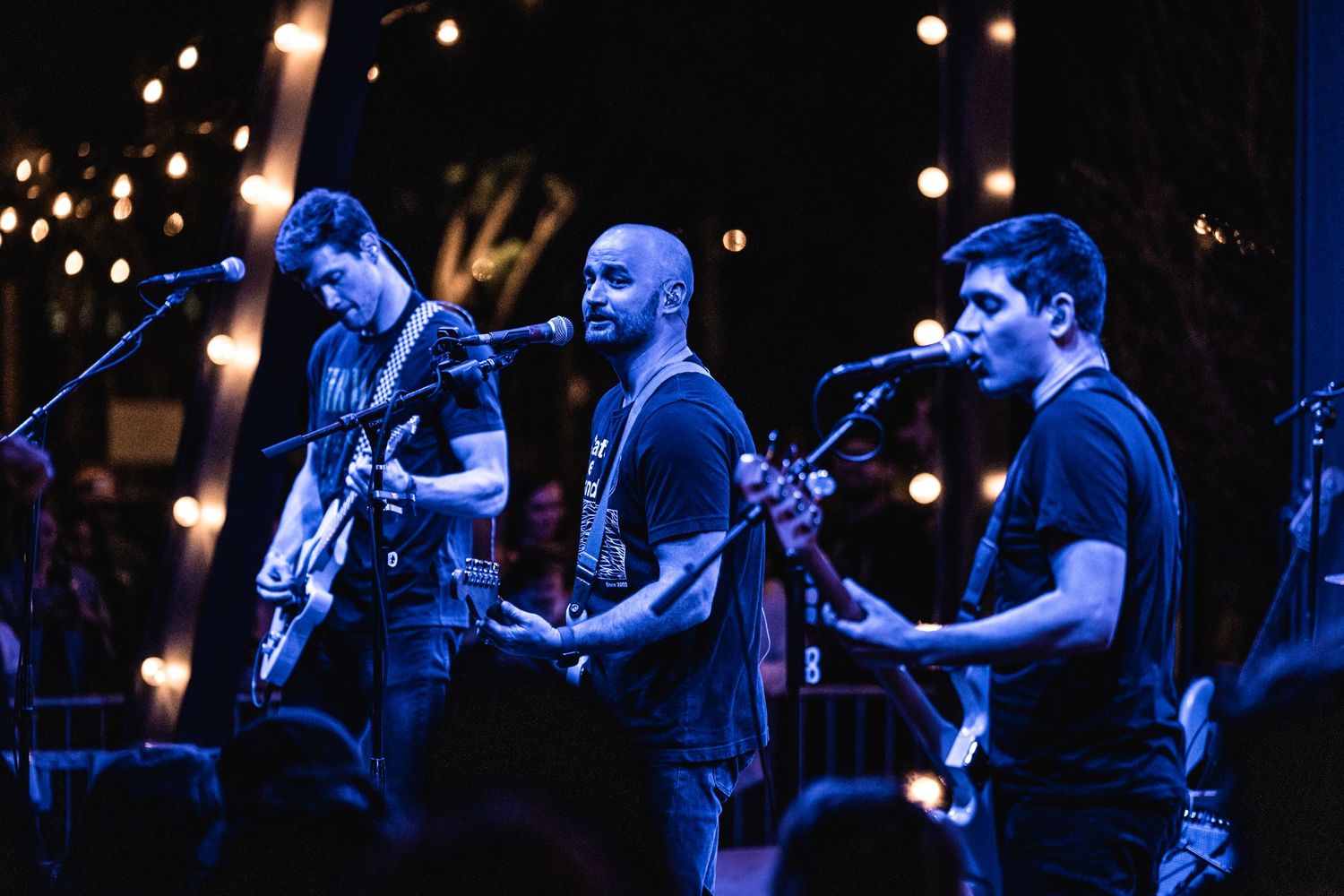 Musicians perform together on darkened stage with blue lighting effects.