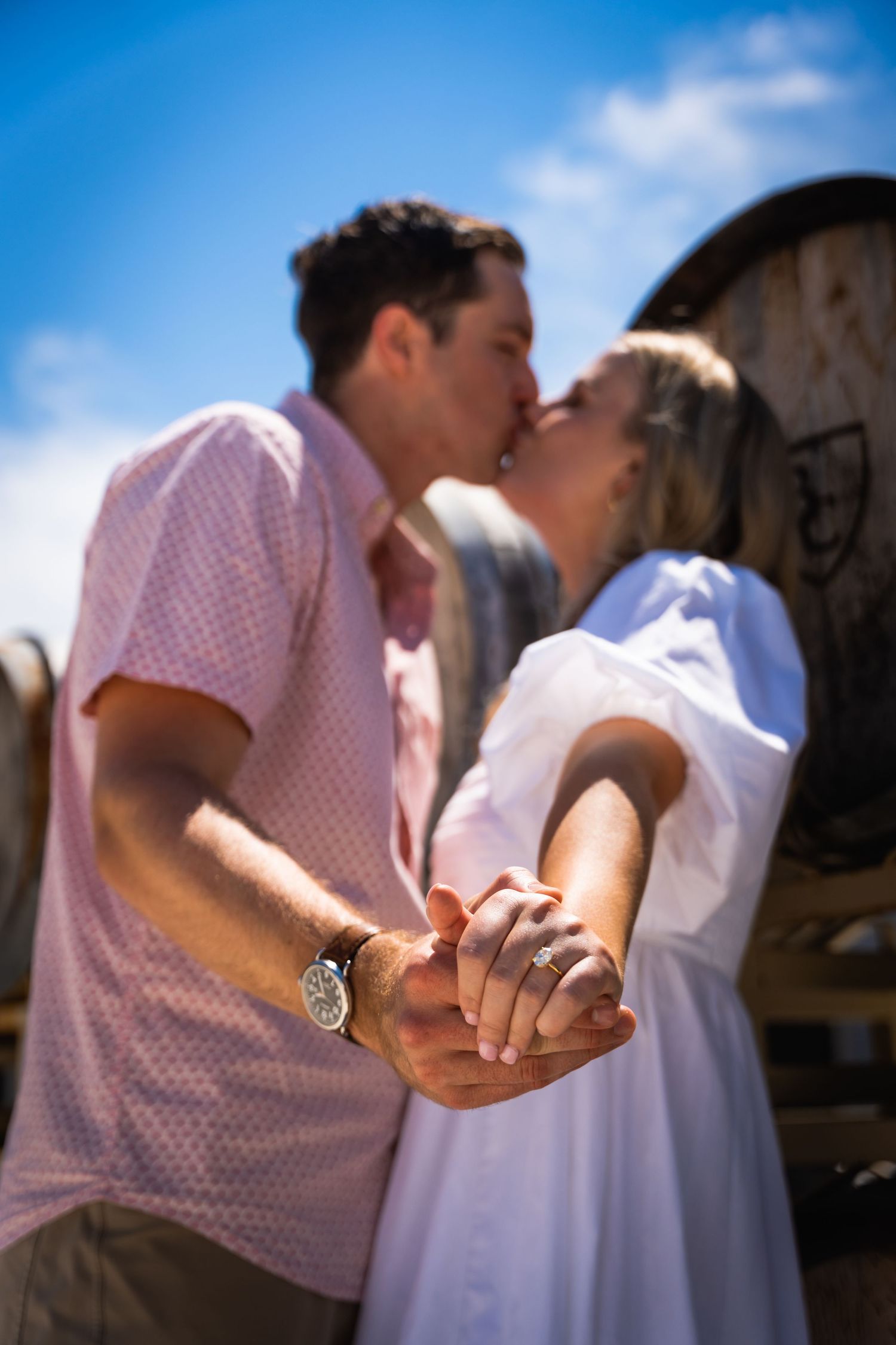 A tender moment captured between a couple holding hands in front of wine barrels.