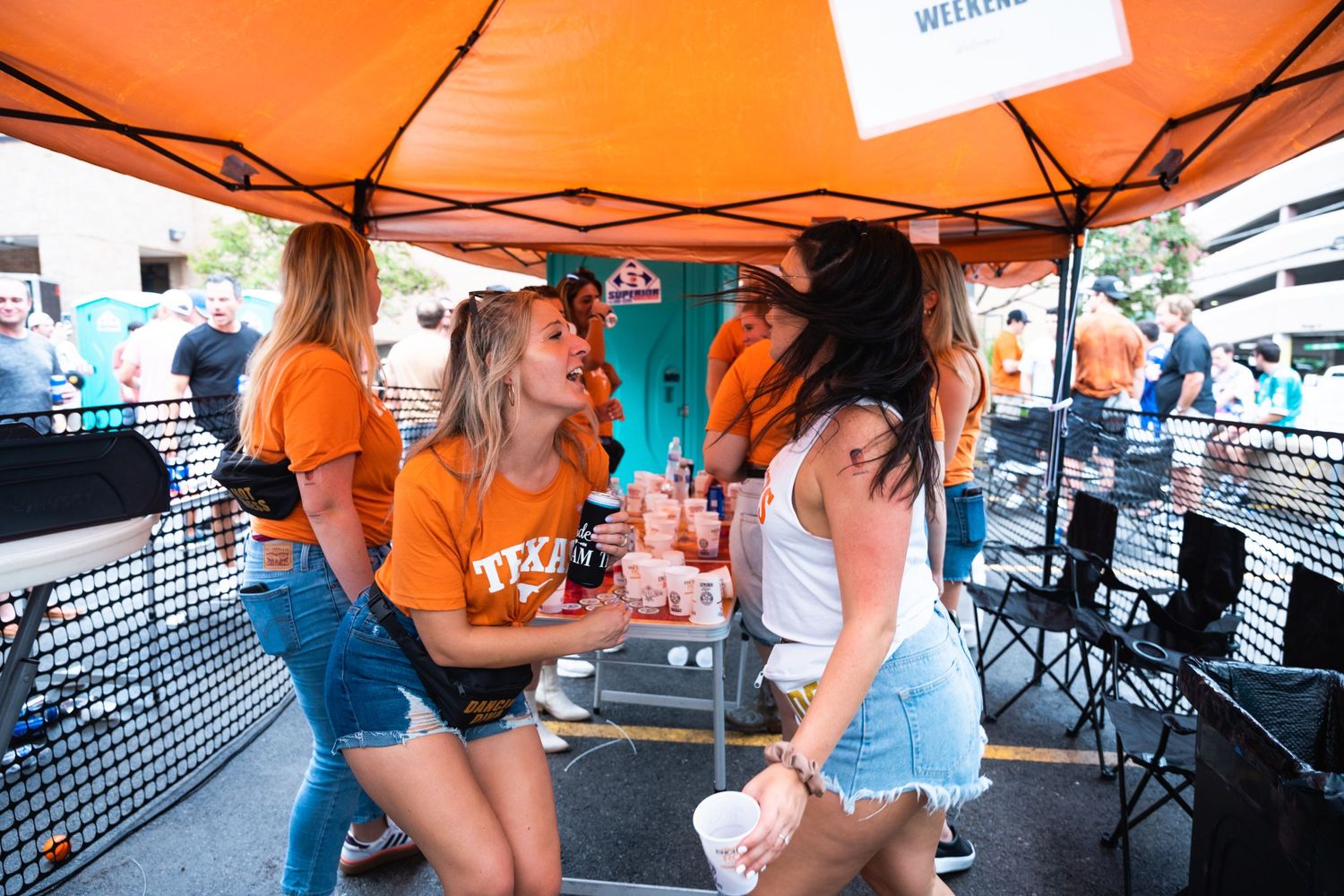 Women in orange shirts socializing and having drinks under a vibrant orange tent.