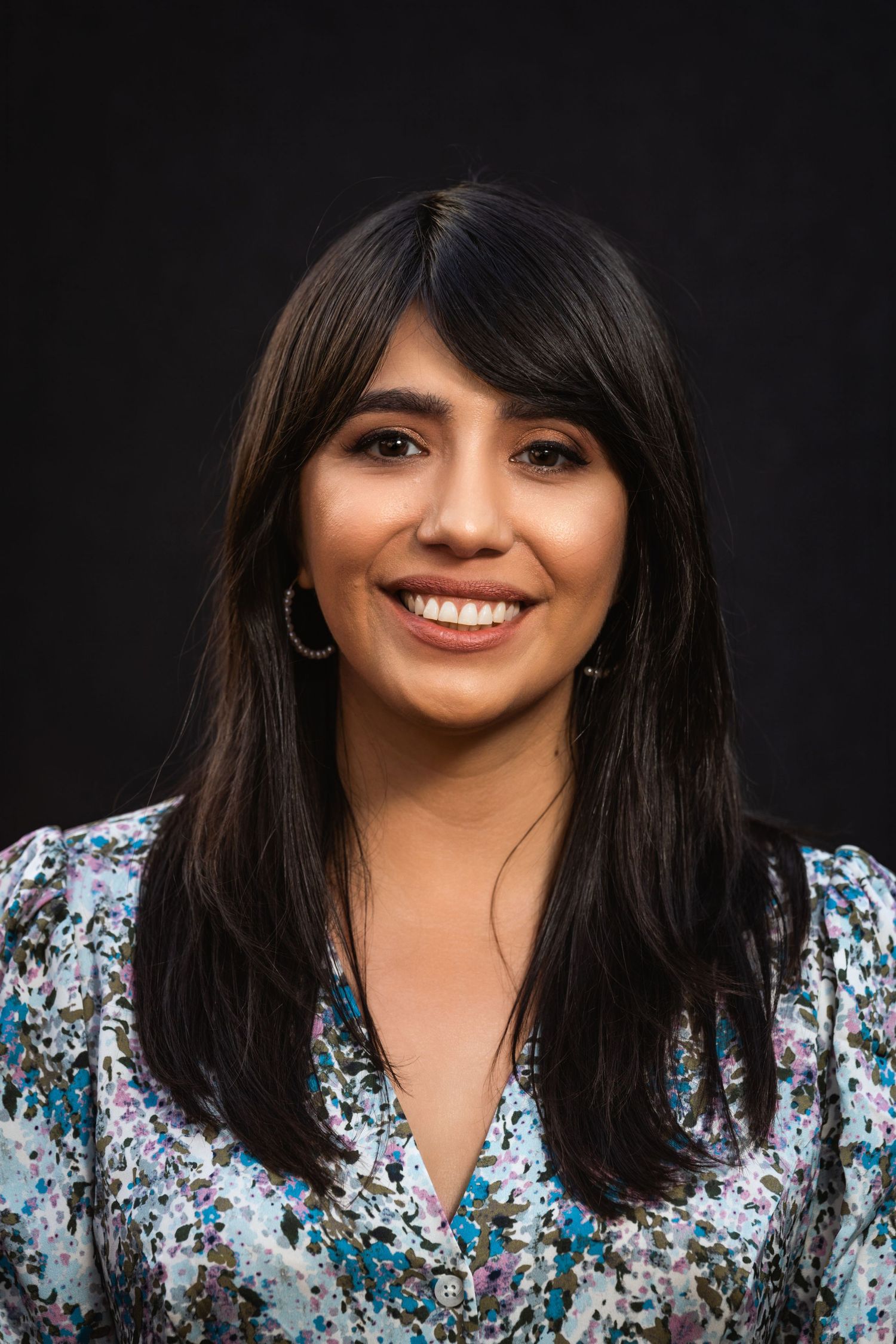 Studio portrait with person wearing floral patterned top and silver earrings against black backdrop.