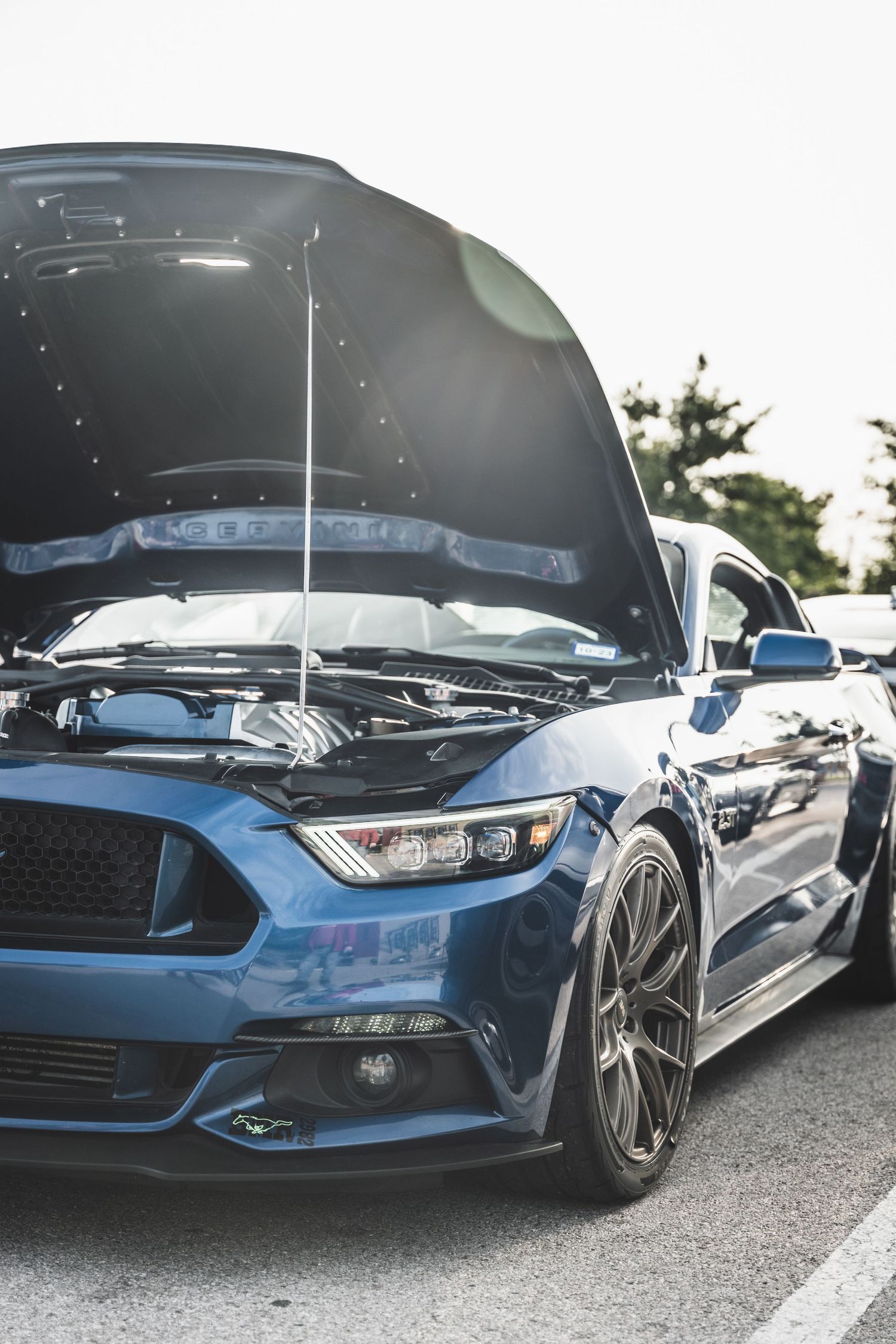 A blue Ford Mustang with its hood open displaying the engine bay at a car show.