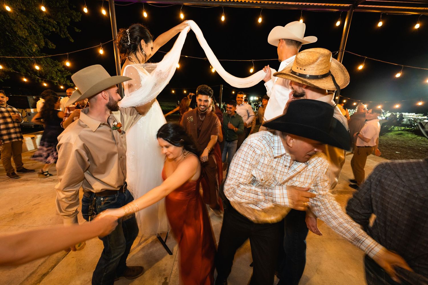 A lively dance circle forms under string lights at an outdoor western-themed celebration.