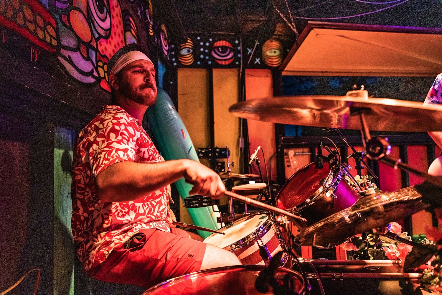 Drummer performing on stage with colorful lighting and concert atmosphere.