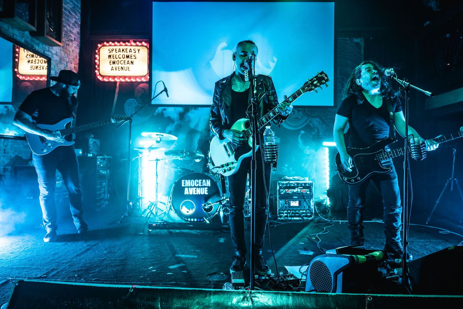 Rock band performs on stage with blue lighting and vintage marquee signs in background.