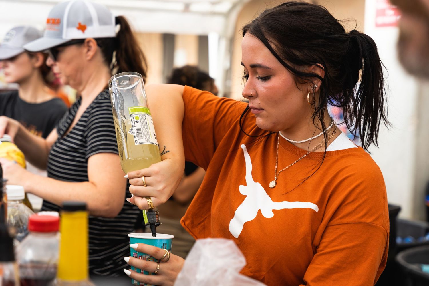 Person in orange Texas Longhorns shirt pours a drink at an outdoor event.