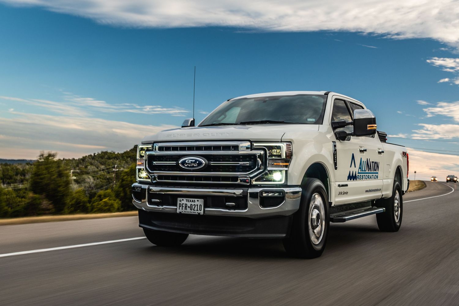 White Ford F-250 pickup truck driving on a scenic road against blue sky.
