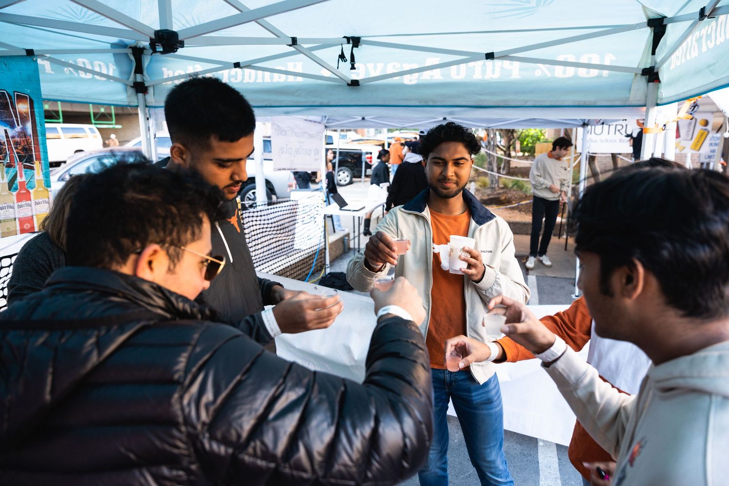 Group of friends sharing food and drinks under a white canopy tent.