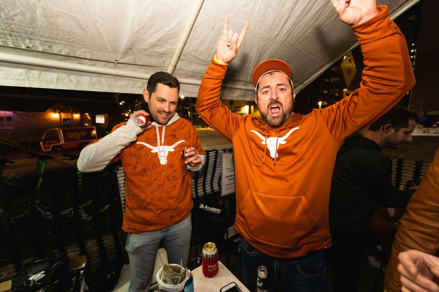 Two people in matching orange hoodies celebrating and gesturing excitedly.