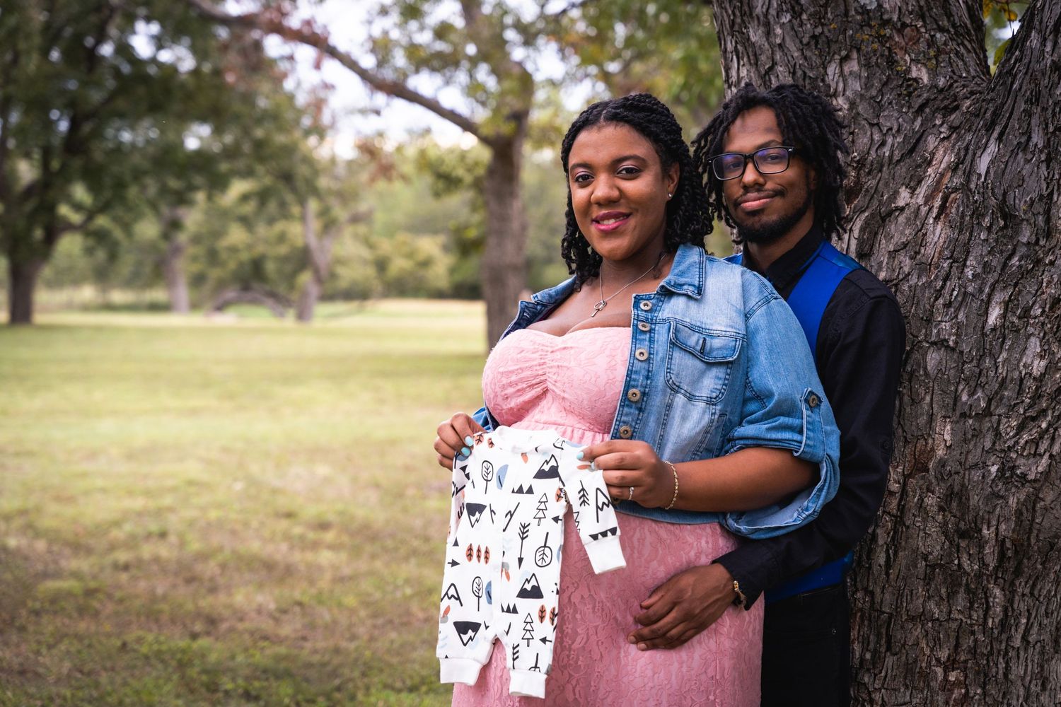 A maternity photo session under a large tree with couple holding pregnancy-themed props.