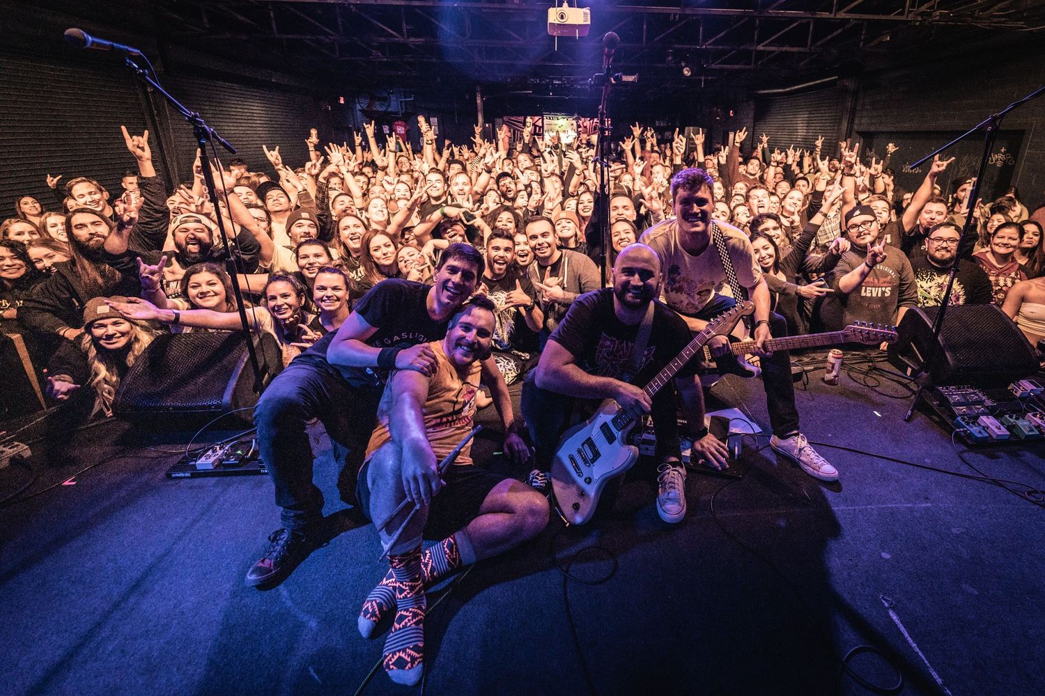 Packed concert venue with crowd and performers posing together for group photo.