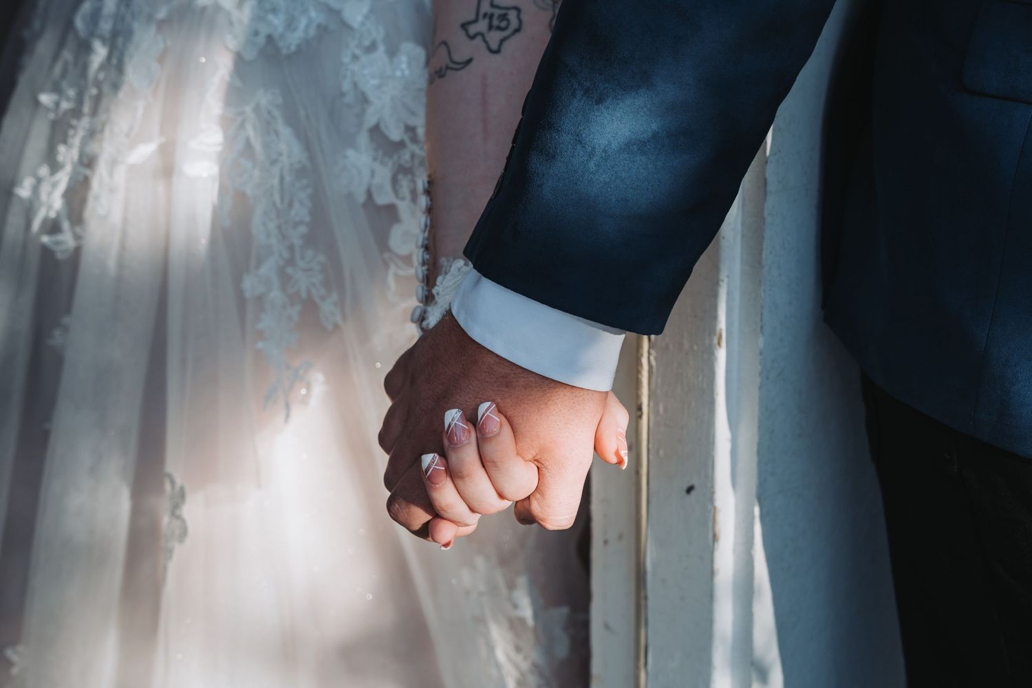 Close up shot of newlyweds holding hands showing wedding attire details.