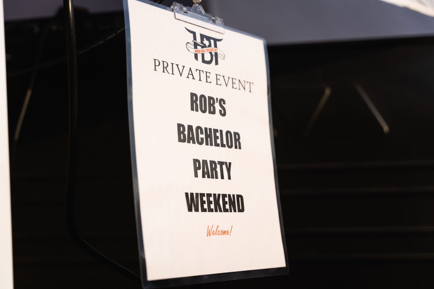 A black and white event sign for a bachelor party weekend mounted on a post.