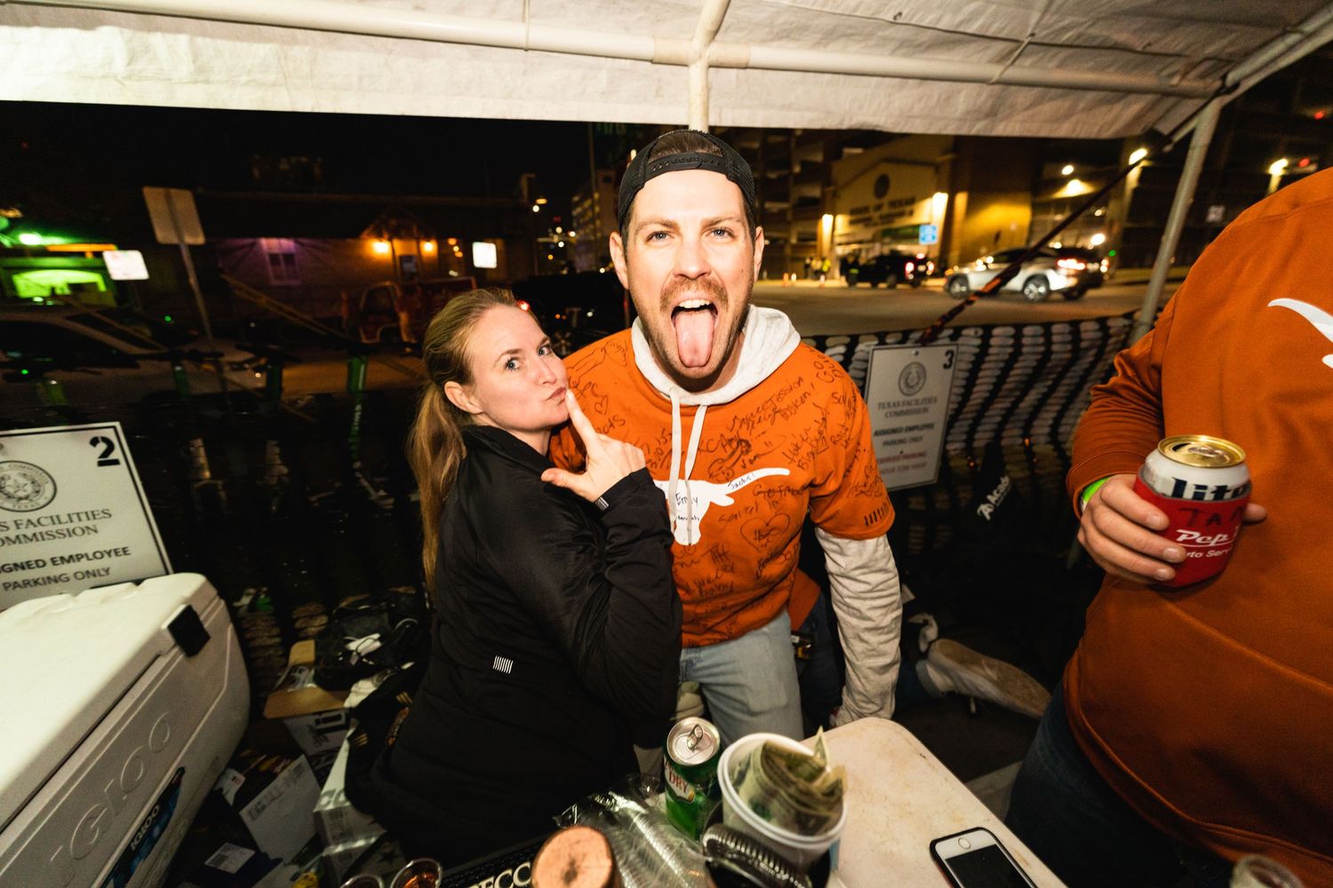 Couple sharing a playful moment at outdoor gathering with orange University of Texas gear.