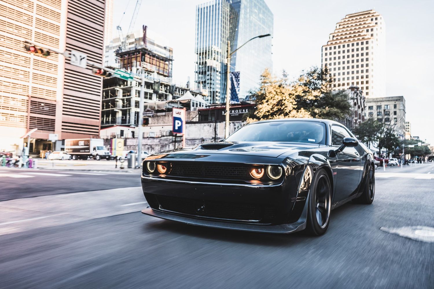 Modified black Dodge Challenger driving on city street with illuminated orange headlights.