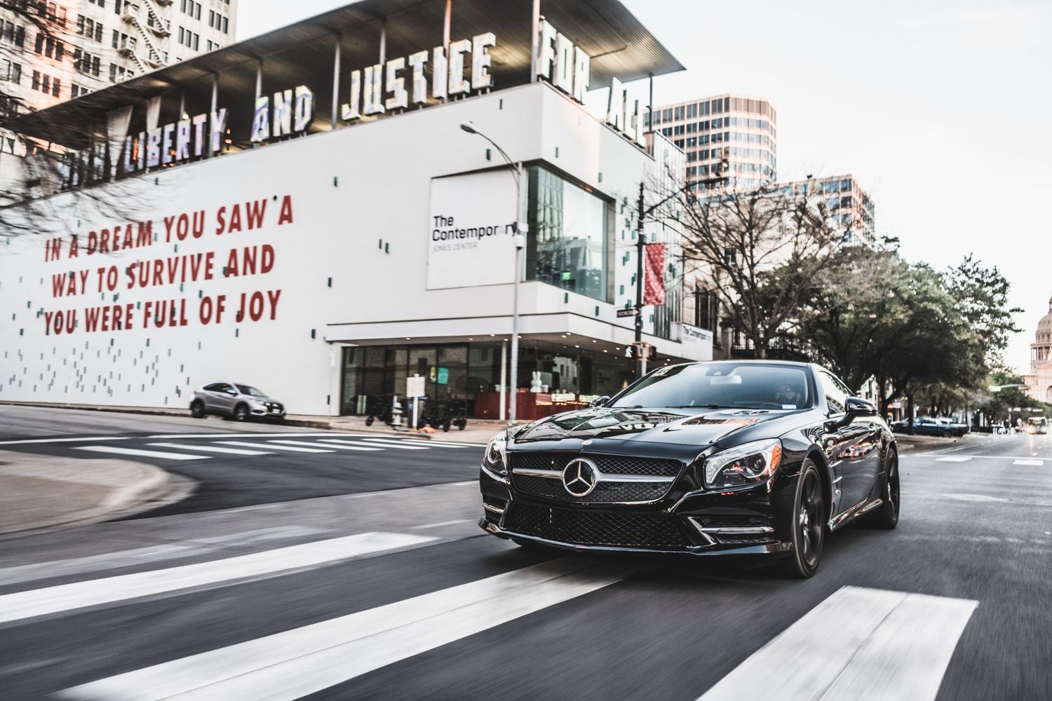 Black Mercedes coupe parked near street art mural in urban setting.