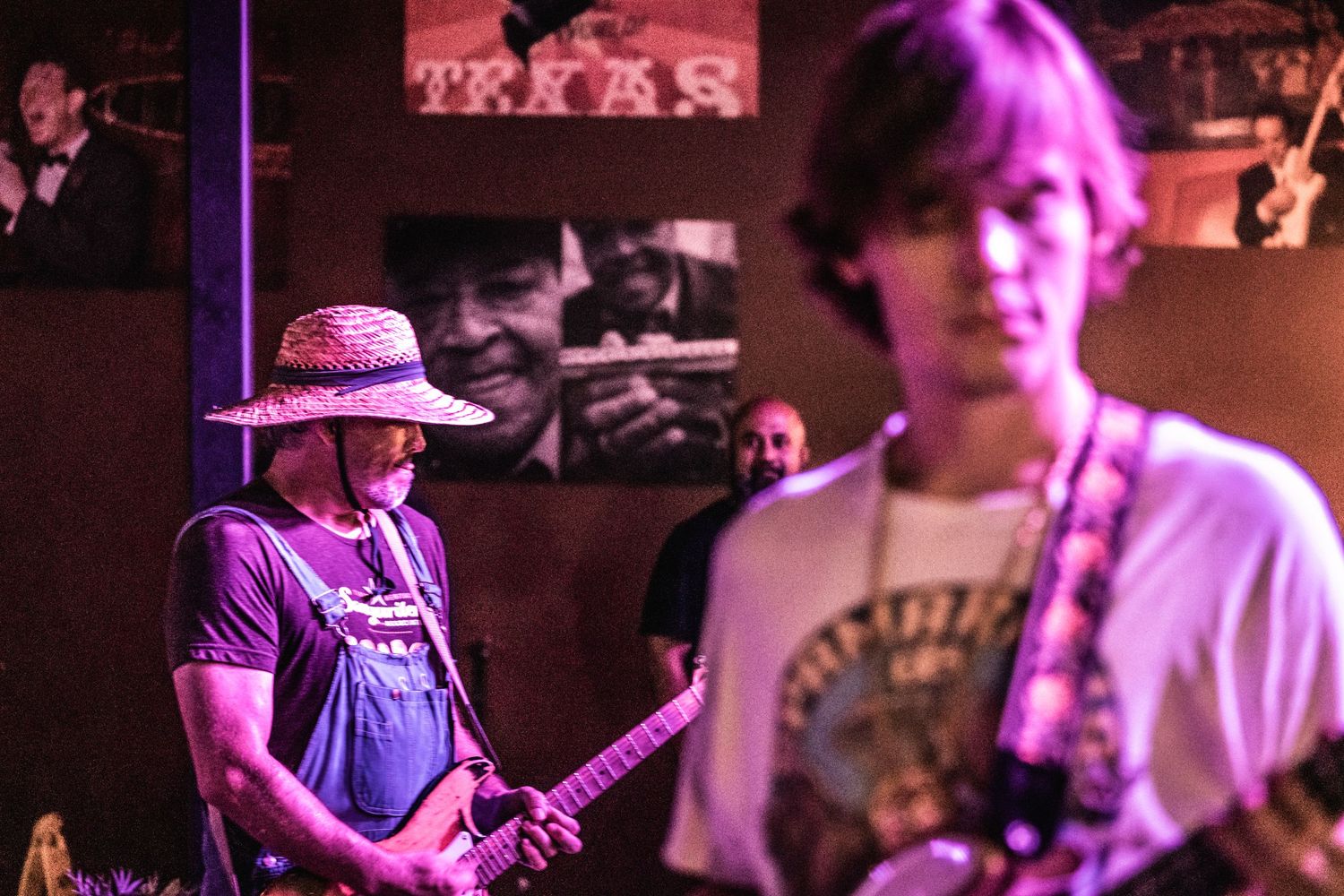 Musicians with guitars performing on stage with Texas-themed wall decorations in the background.