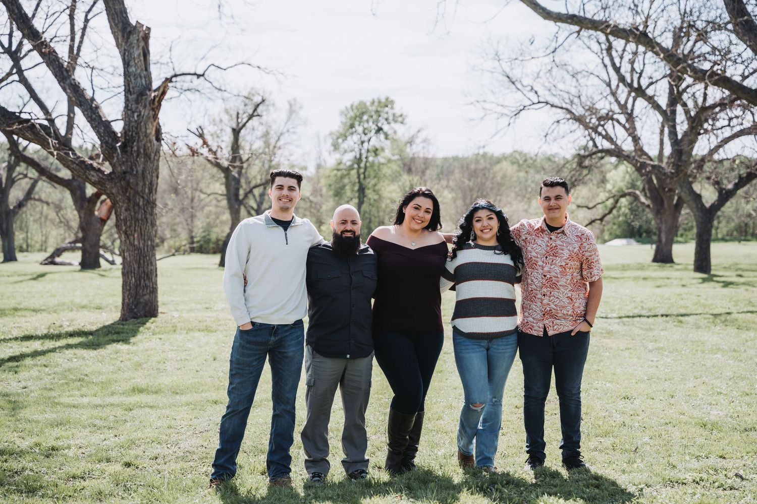 Group photo of five people posing together in an open field with trees in the background.