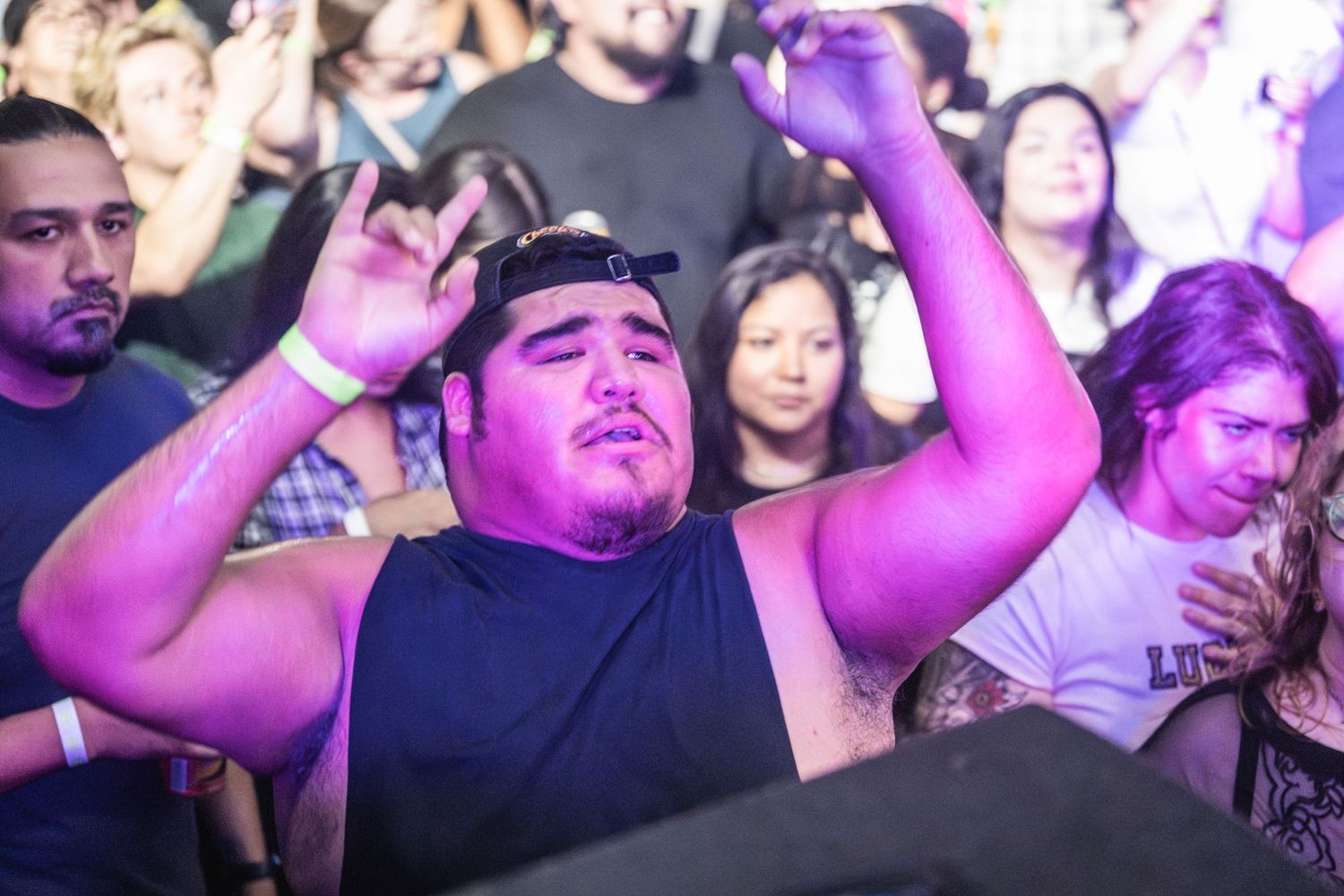 Crowd of concert attendees dancing and raising hands during a live music performance under purple stage lighting.