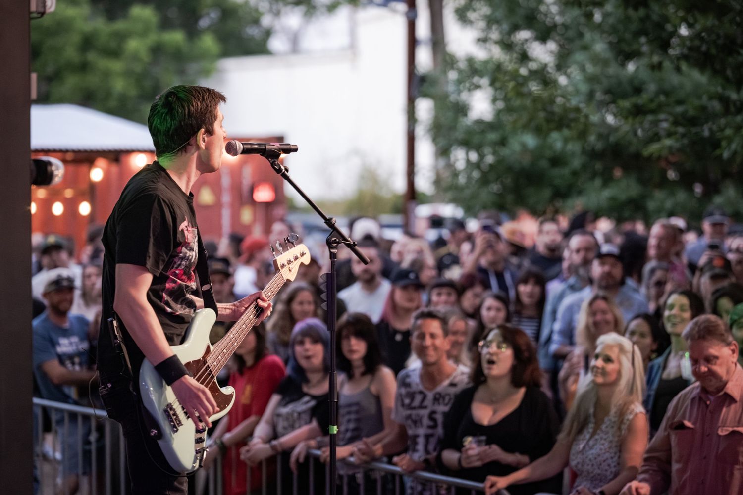 Guitarist performs on outdoor stage at dusk before a large crowd at a live music festival.