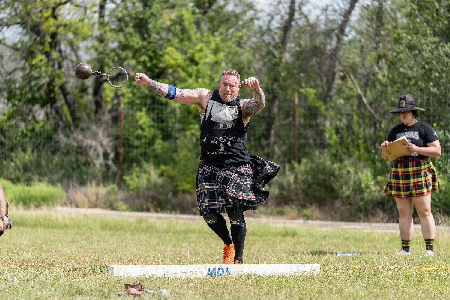 Athlete in tartan kilt competes in Highland Games throwing event outdoors.