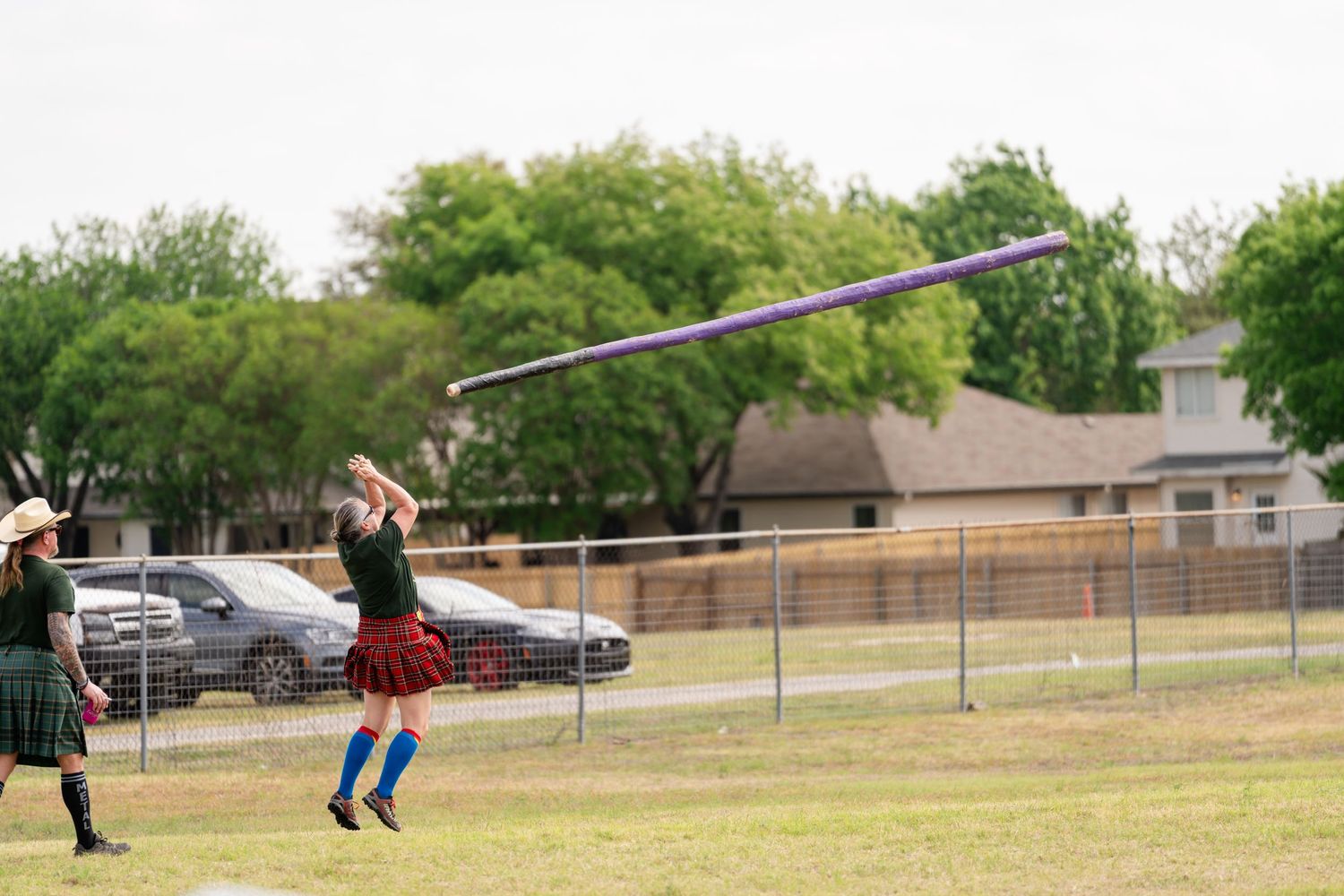 Woman in traditional Scottish Highland Games attire throwing a javelin on a green field outdoors.