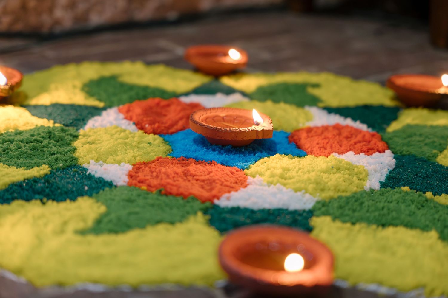 Colorful sand art rangoli design illuminated by small clay oil lamps for Diwali festival celebration.