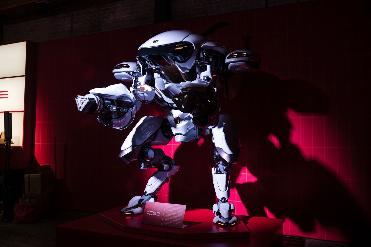 A large robotic mech suit illuminated by dramatic red and blue lighting stands in a dark exhibition space.
