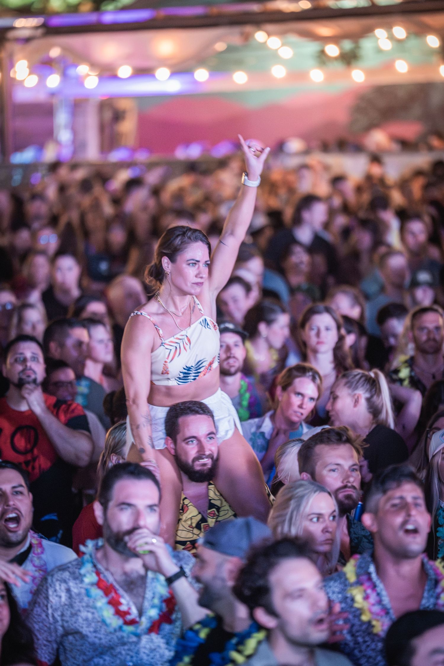 A large crowd of excited concert-goers cheers and raises their hands during a live music performance.