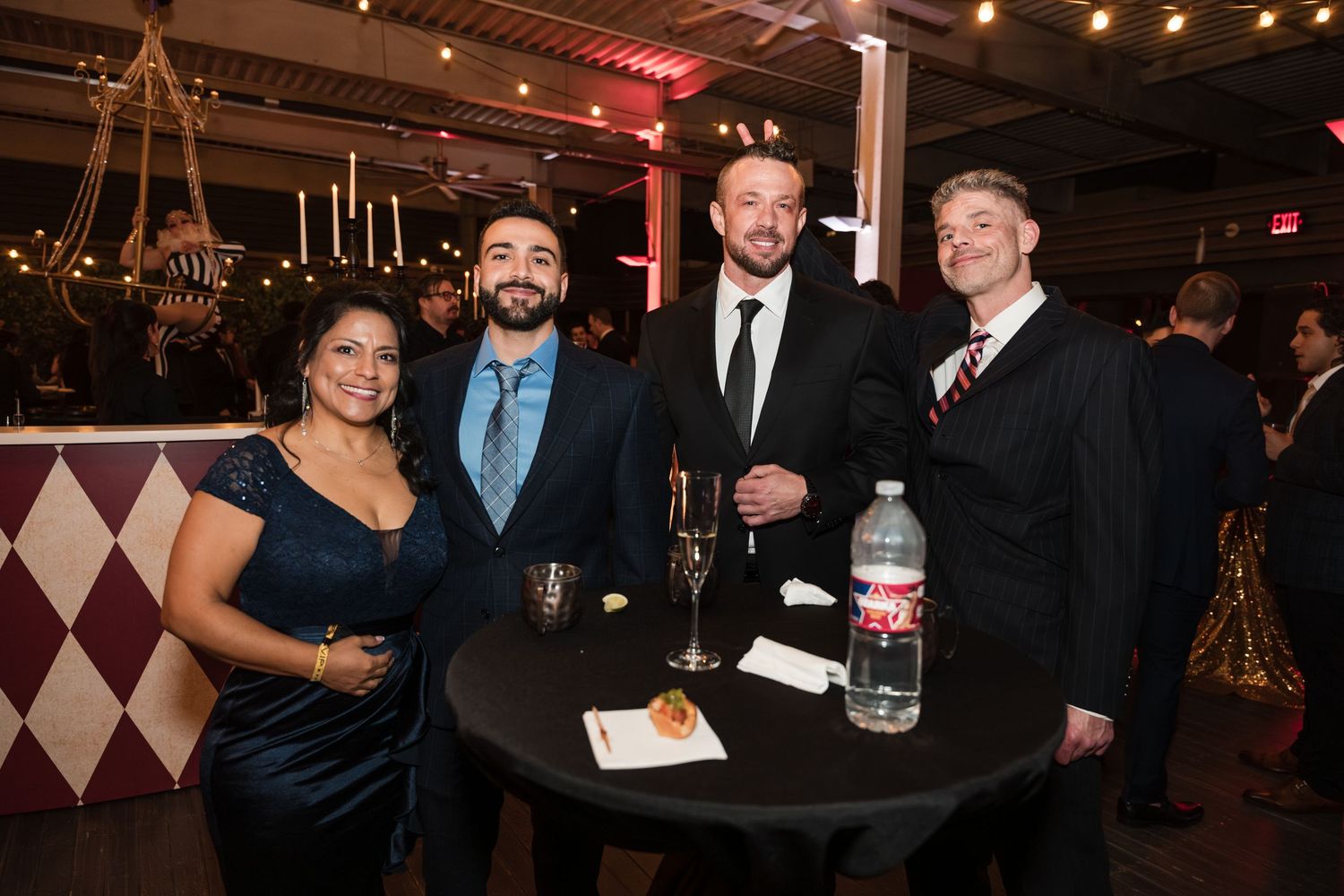 People mingling at an elegant evening event with dark decor and ambient lighting.