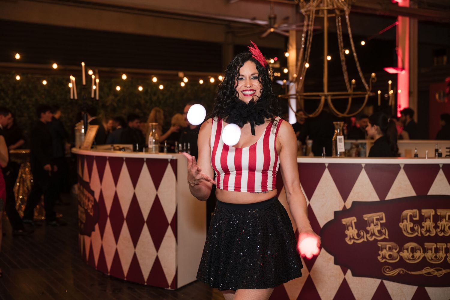 A nightclub interior with checkered walls and chandeliers features performers entertaining guests on stage.