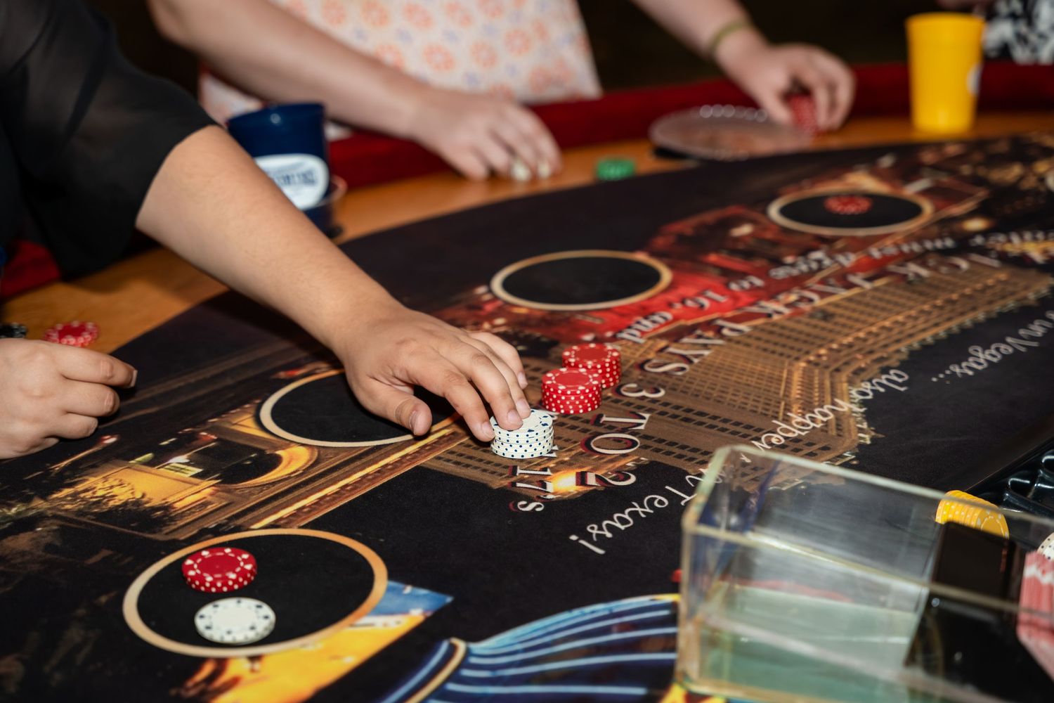 Close-up view of hands playing poker at a casino table with chips and cards spread out on the felt surface.