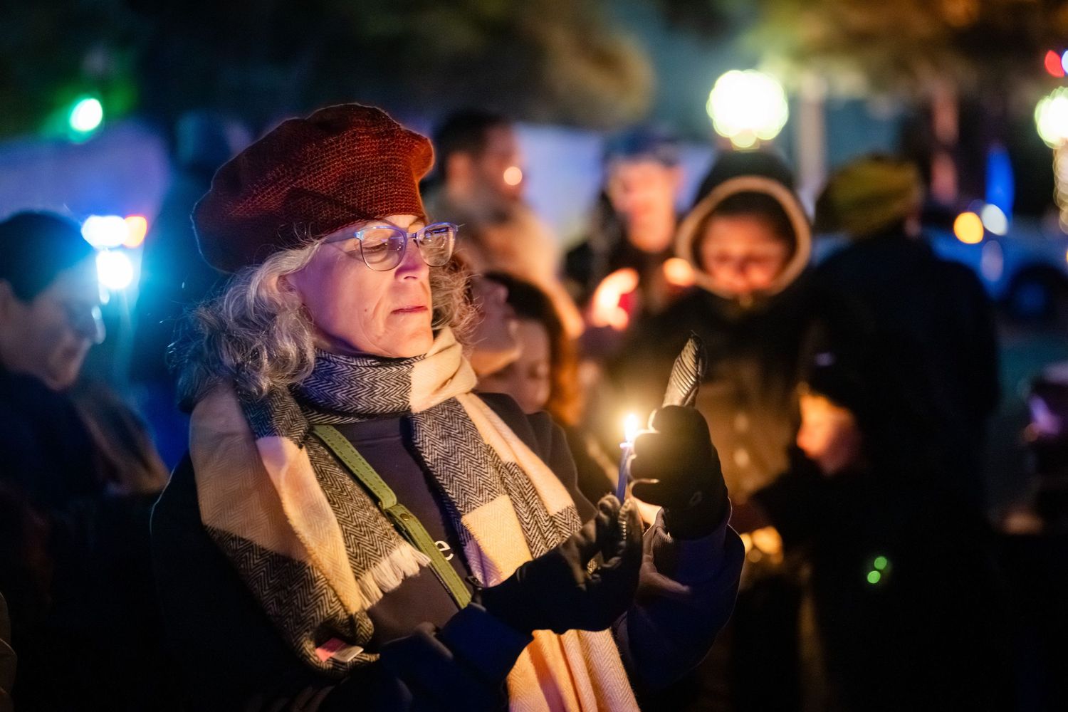 People hold glowing candles during a nighttime vigil gathering in a dark outdoor setting.