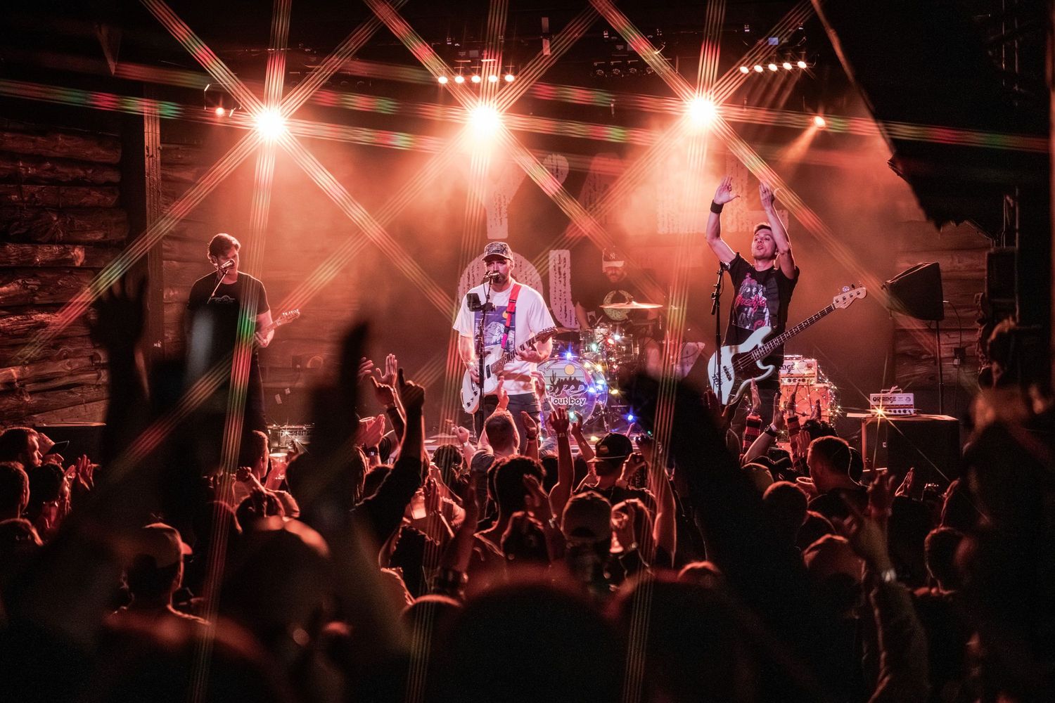Concert crowd cheers enthusiastically during a live performance with red stage lighting and musicians on stage.