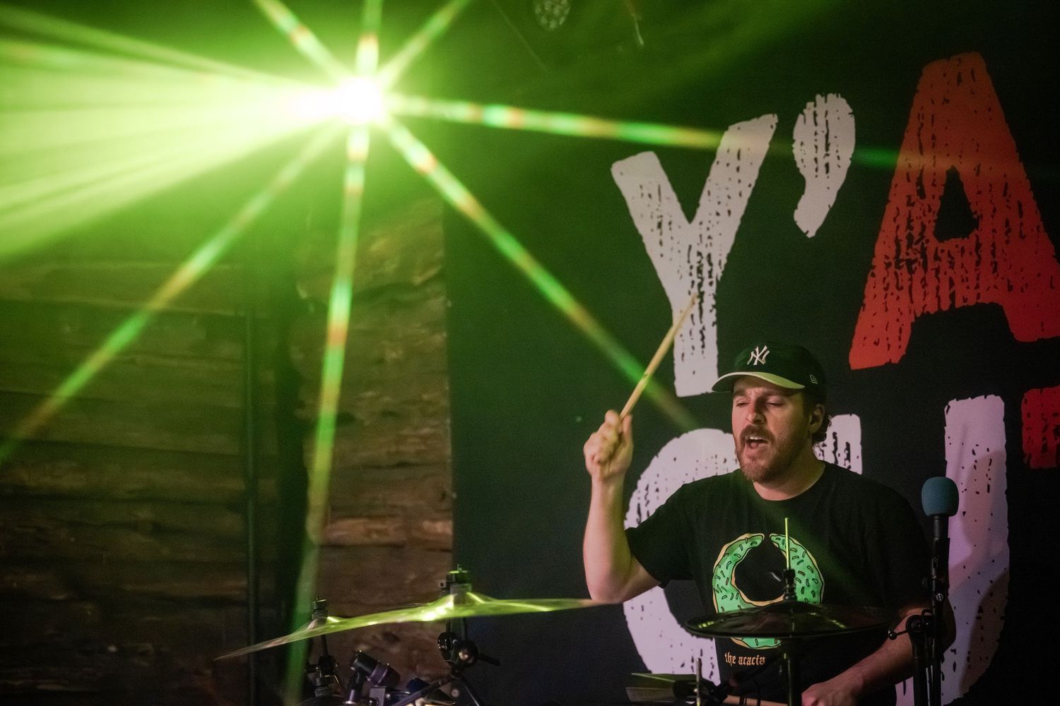 A performer stands on stage with dramatic green lighting and effects during a live music performance.