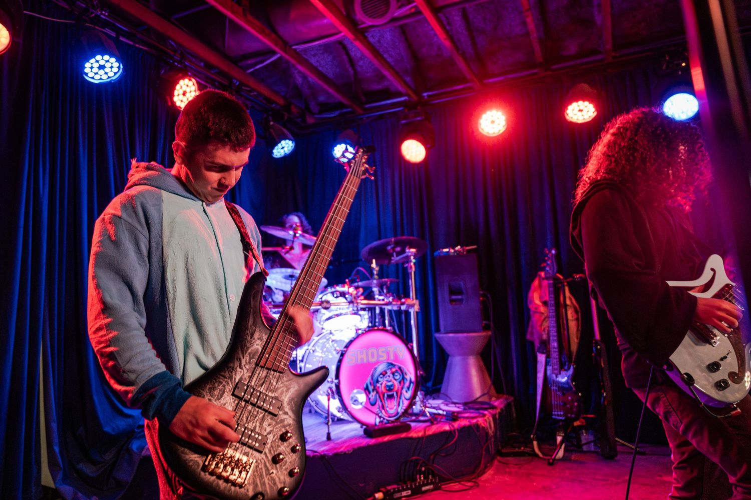 Musicians perform on stage at a concert venue illuminated by vibrant red and blue lighting.