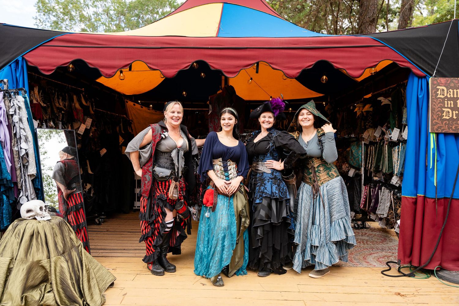 A colorful row of vendor tents and stalls at a Renaissance festival with medieval costumes and decorations on display.