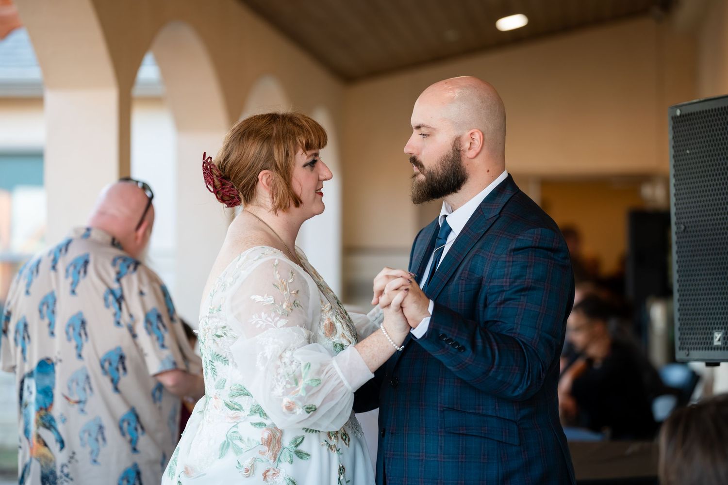 A couple dances together at a wedding reception, with the bride wearing a white lace dress and groom in a navy suit.
