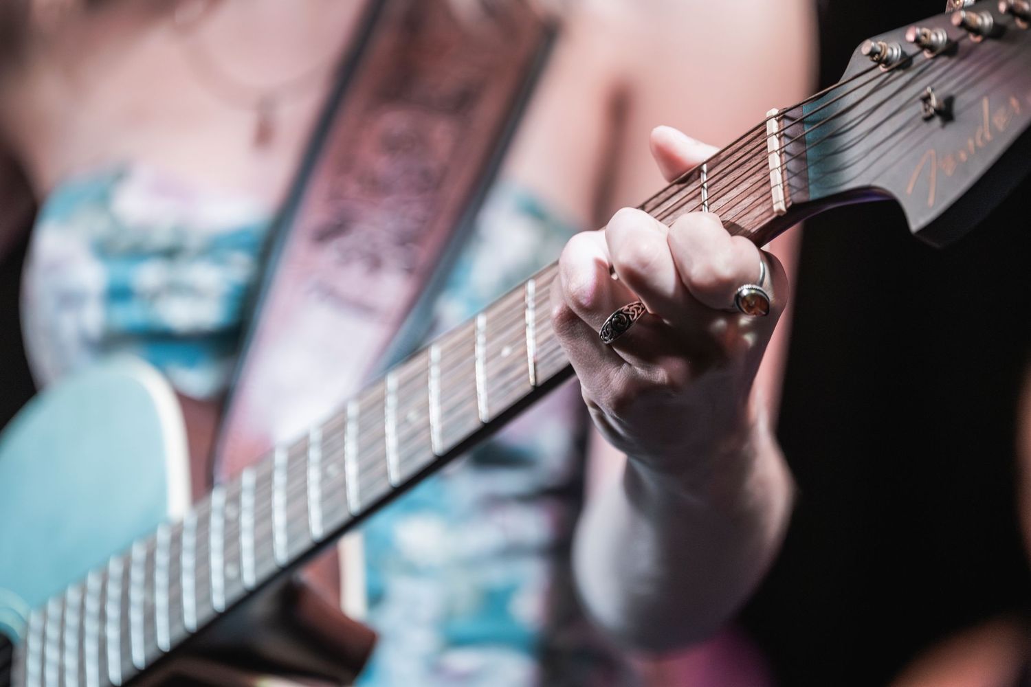 Close-up shots of hands playing electric guitar strings and fretboard with colorful lighting effects in the background.