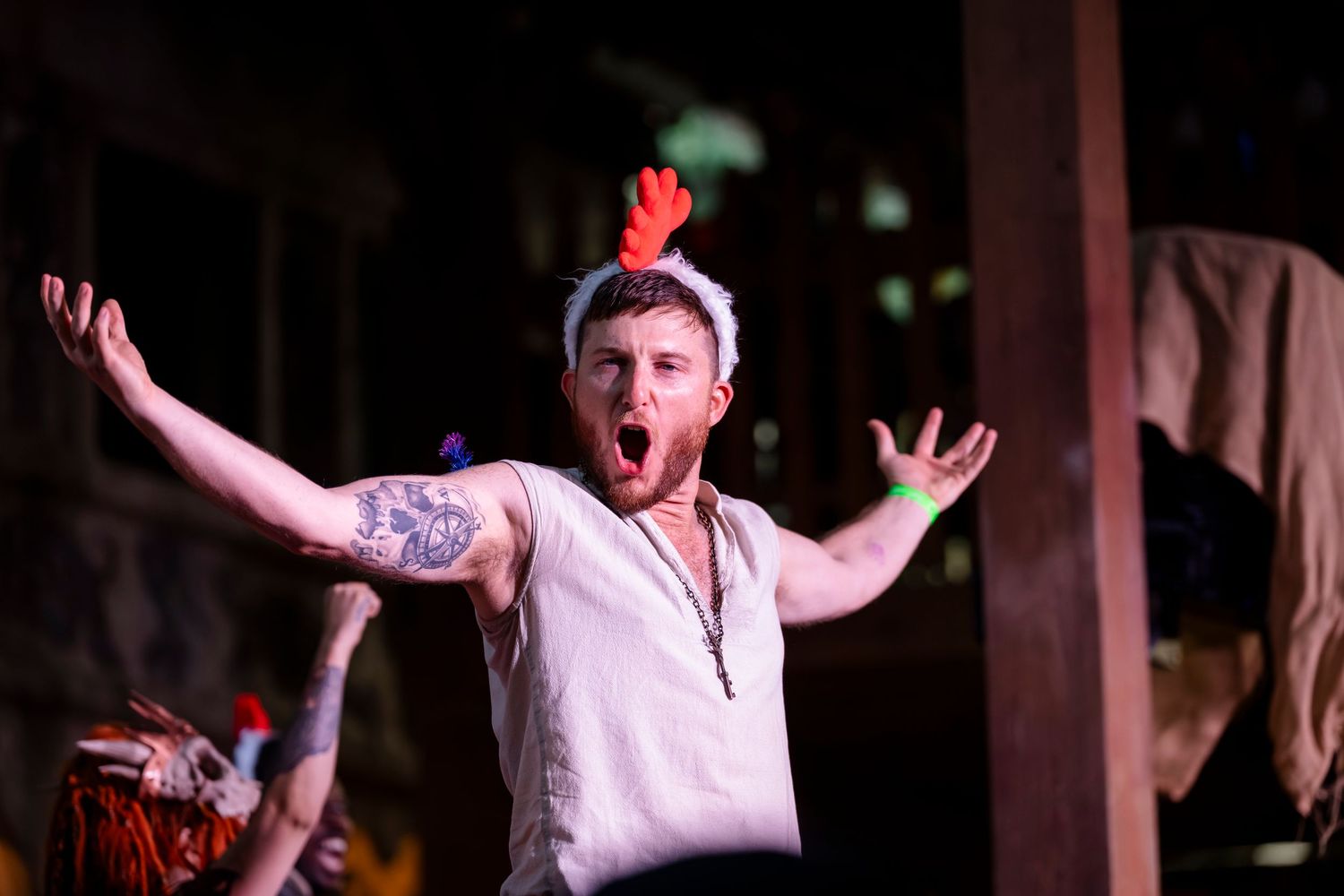 Energetic performer in white tank top spreads arms wide while singing passionately on stage during live performance.
