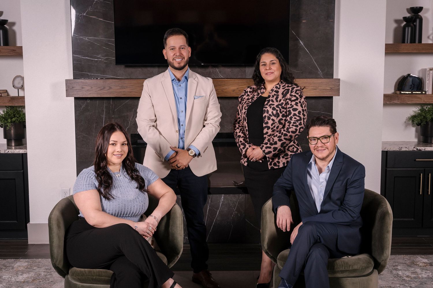 Professional business team sitting and standing in front of a modern fireplace in a living room setting.