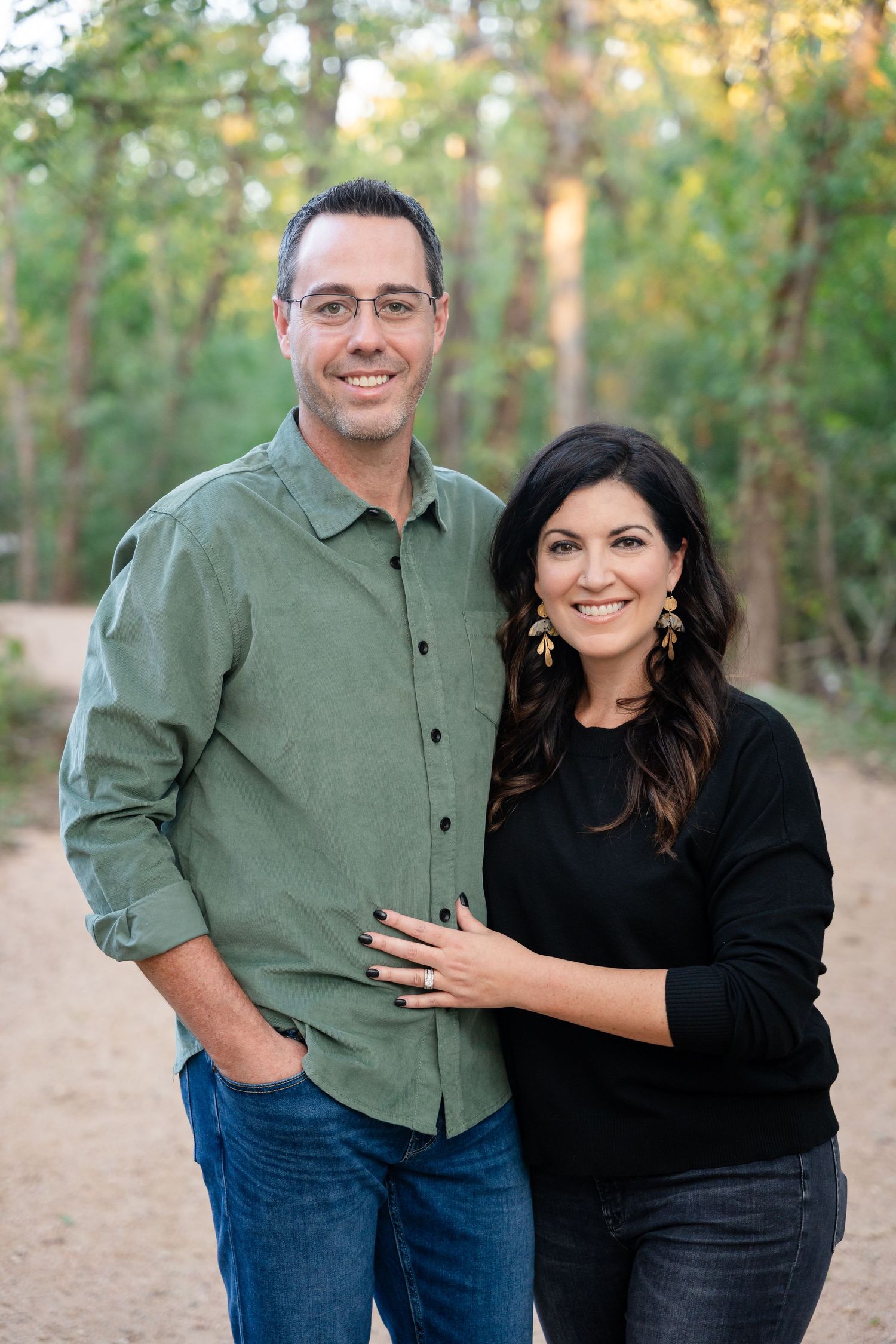 A couple poses together on a nature trail surrounded by autumn trees.