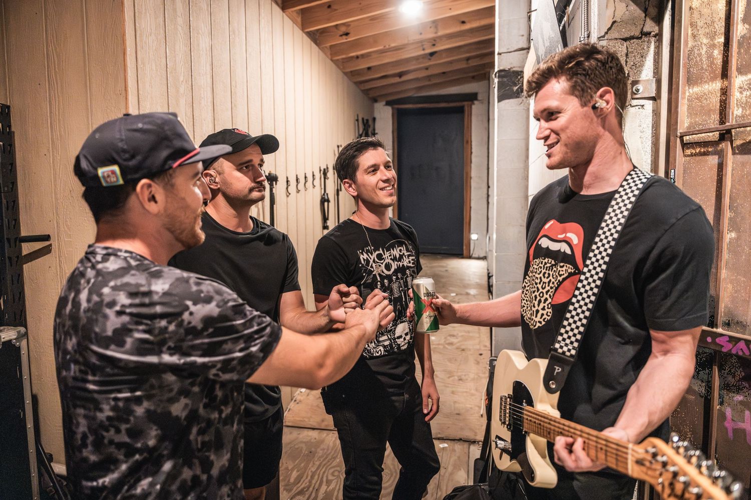 Musicians socializing backstage in a wooden-paneled room before a performance.