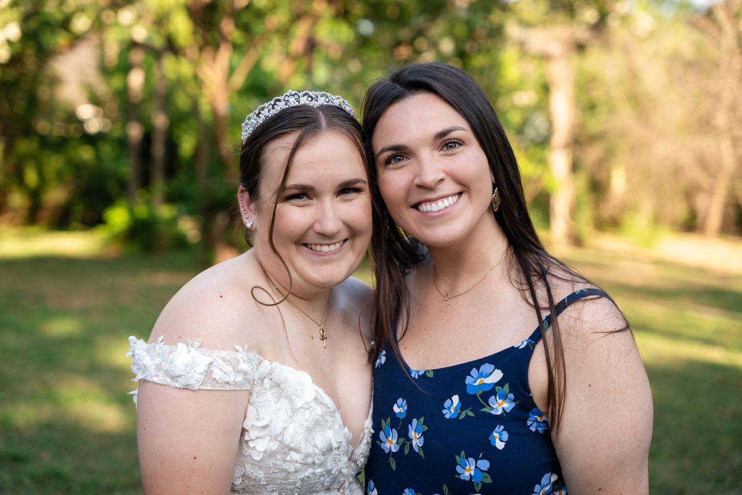 Two wedding guests share joyful moment outdoors with natural greenery in background.